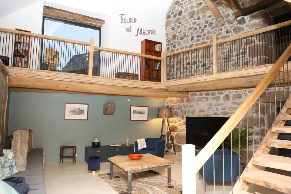 Grand séjour avec mezzanine en bois et mur de pierre