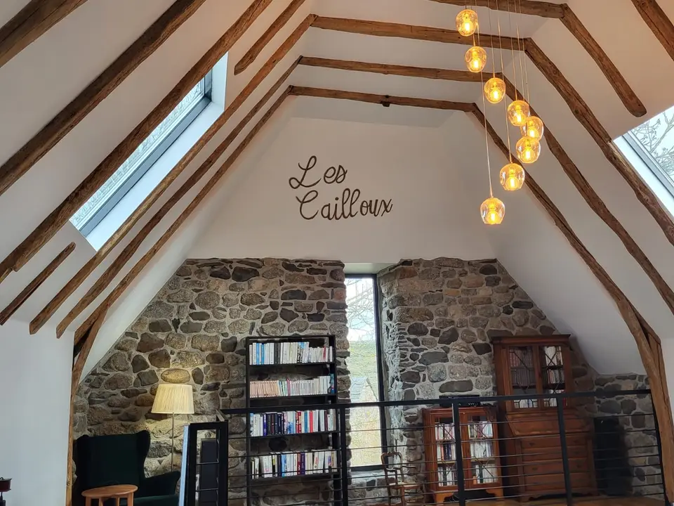 Coin bibliothèque sous la charpente, devant un mur de pierre